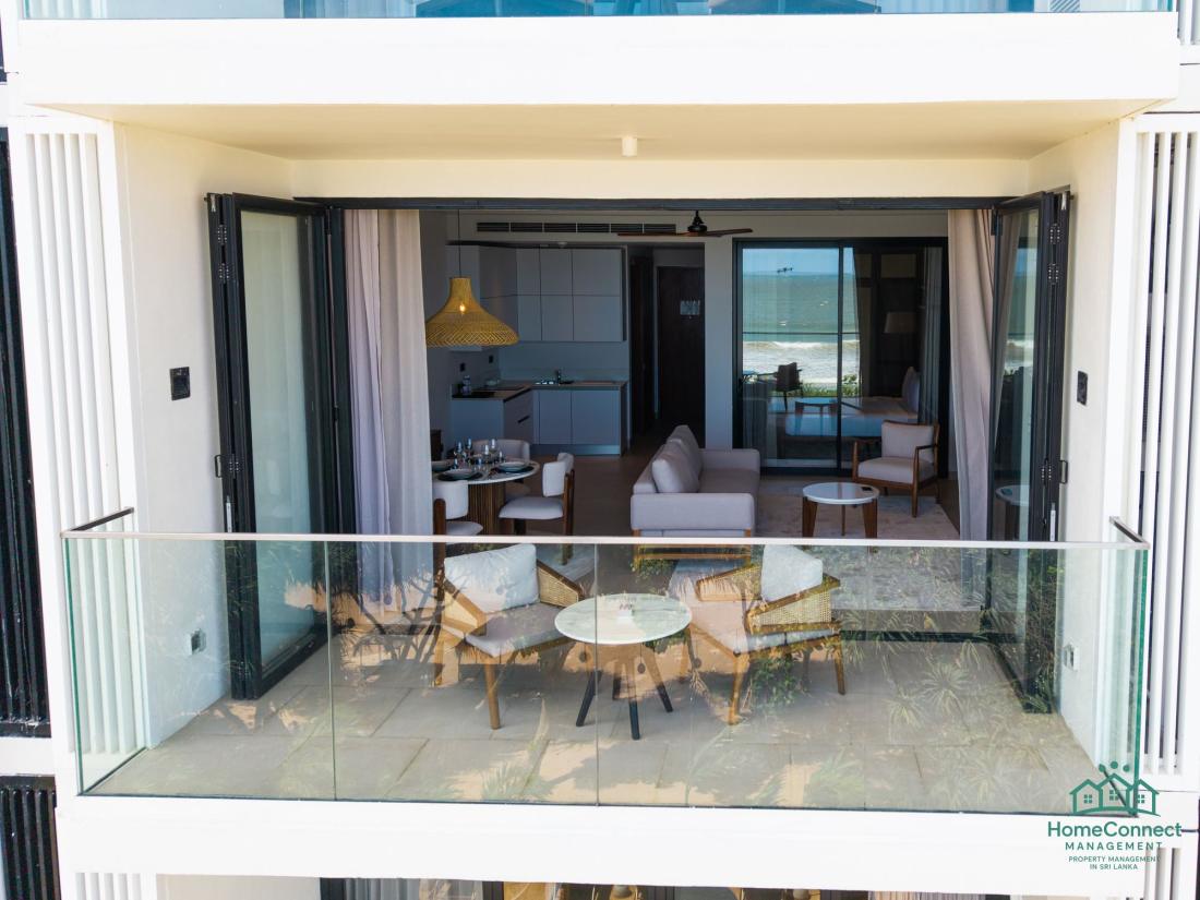 Folding doors open from a balcony into a furnished HomeConnect living room facing the sea