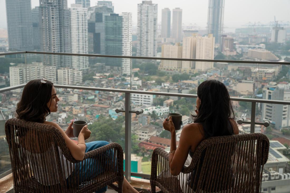 Two women with coffee on a high-rise balcony above the Colombo skyline